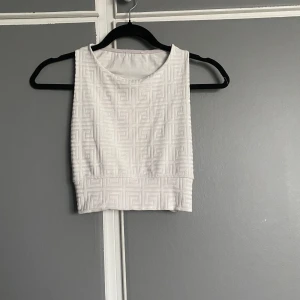 Vit mönstrad croppad linnetopp - Säljer en snygg vit croppad linnetopp med ett diskret geometriskt mönster. Toppen är ärmlös och perfekt för sommardagar eller som ett lager under en jacka. Den har en bekväm passform och är gjord i ett mjukt material. Perfekt för en avslappnad stil eller en dag på stan!