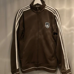 Vintage Adidas Tracksuit Storlek Medium - En Hamburg track jacket från adidas. Tröjan är ifrån FIFA World Cup 2006. Jätte fet brun färg med dom klassiska 3 ränderna i vitt längst armarna 😎