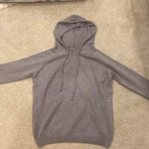 Grå hoodie - Säljer en stilren grå hoodie i mycket bra skick. Den är perfekt för både höst och vinter med sin mjuka och bekväma passform. Hoodien har långa ärmar och en klassisk huva med dragsko. Perfekt för mysiga dagar eller en avslappnad stil. Passar 170-180 och helt ny material är Kashmir