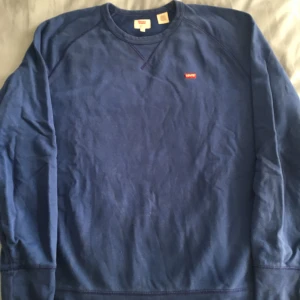 Blå sweatshirt från Levi's - Säljer en snygg blå sweatshirt från Levi's i storlek M. Tröjan har en klassisk design med rund hals och långa ärmar, rätt bred modell. Perfekt för en avslappnad stil och passar bra till både jeans och chinos. Levi's-loggan syns diskret på bröstet. 