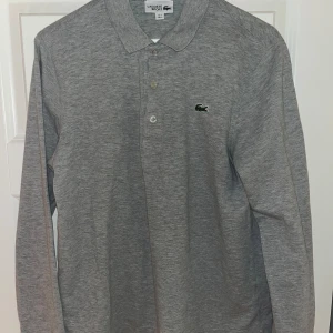 Lacoste long sleeve grey - Säljer denna grå Lacoste polo-tröja, longsleeve med knappar. Då den börjar bli för liten för mig. Endast använd 2 gånger så kvalitet är mycket bra (10/10). Storlek M men är liten i storleken.