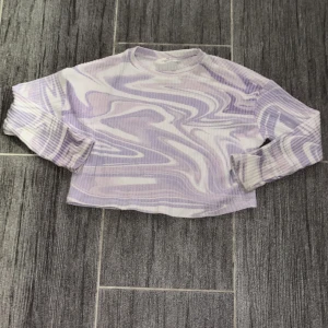 Lila och vit mönstrad tröja från H&M - Säljer en superfin lila och vit tröja från H&M med ett coolt mönster. Tröjan är croppad. Den är i mycket bra skick och passar perfekt till ett par jeans eller shorts. 