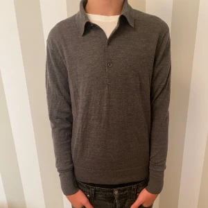 Grå pikétröja från Uniqlo - Säljer en stilren grå pikétröja från Uniqlo i storlek XS. Tröjan har långa ärmar och en klassisk krage med knappar framtill. Den är i 100% merinoull. Modellen är 176
