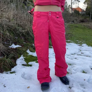 Rosa byxor med fickor - Snygga rosa byxor med flera praktiska fickor och knappdetaljer. Perfekta för en färgglad och bekväm stil. Byxorna har en lös passform och är ideal för sportlovet när man går på afterski  