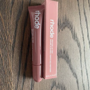 Rhode Peptide Lip Tint - Rhode Peptide Lip Tint i färgen ”toast”. Denna läpprodukt kommer i en praktisk tub och är designad för att ge både färg och vård till läpparna. 