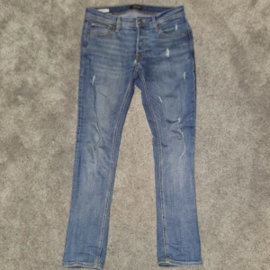 Blå jeans från Jack & Jones - Snygga blå jeans från Jack & Jones i modellen Slim/Glenn. De har en slim passform och är tillverkade i denim med slitna detaljer för en trendig look. Perfekta för en avslappnad stil. Inte i perfekt skick med tanke på att den taggen där bak är bortagen