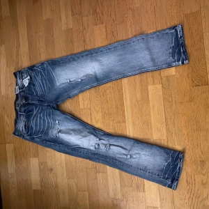 Blå jeans med slitningar - Snygga blå jeans med coola slitningar och en klassisk femficksdesign. De har en knapp och dragkedja framtill. Perfekta för en avslappnad stil. MIDJA 34 LÄNGD 32