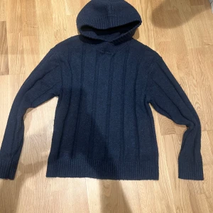 Mörkgrå stickad hoodie från Zara - Säljer en snygg mörkgrå stickad hoodie från Zara. Tröjan har en ribbad struktur och långa ärmar, perfekt för kyliga dagar. Den har en bekväm huva och är gjord i ett mjukt material som håller dig varm. Passar perfekt till både jeans och avslappnade byxor. Väldigt fint skick och riktigt gött material 