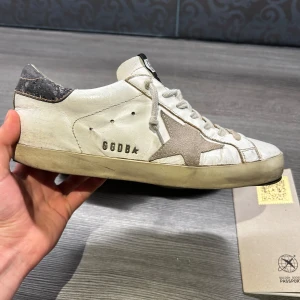 Vita sneakers från Golden Goose - Säljer ett par vita skor från golden goose till bra pris! För att de börjar bli för små. Skorna är i använt skick och har skrapats lite på sulan (se bild 3) men det läcker inte in vatten och är enkelt att fixa. Goose pass kommer med! Pris kan diskuteras vid snabb affär. Skorna är i storlek 40 men passar runt 40,5