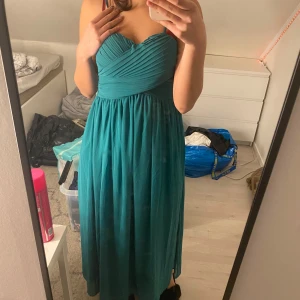 Turkos axelbandslös klänning - Säljer en elegant turkos axelbandslös klänning med veckad överdel och flytande kjol. Perfekt för festliga tillfällen. Klänningen har en smickrande passform och är i en vacker färg som verkligen sticker ut.