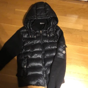 Svart dunjacka från Moncler - Säljer en snygg svart dunjacka från Moncler med huva och dragkedja. Jackan har långa ärmar och en quiltad design på framsidan. Perfekt för kyligare dagar med stil. 🖤