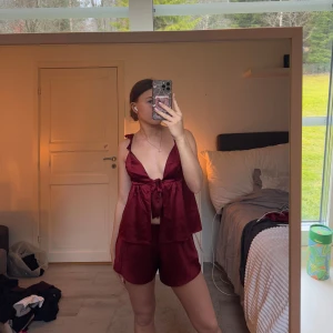 Vinröd set med knytband - Säljer ett snyggt vinrött set med en ärmlös topp och matchande byxor. Toppen har knytband framtill och byxorna är långa för mig som är 164, säljer hela setet med långa-och korta byxor + toppen, slutsålt på Gina och är använde max 1 gång 