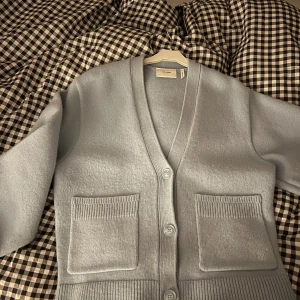 Ljusblå kofta från Axel Arigato - Säljer en stilren ljusblå kofta från Axel Arigato. Koftan har en v-ringad design med knappar framtill och två praktiska fickor. Perfekt för lager-på-lager under kyligare dagar. Ordinarie pris 3000, mitt pris 1500kr