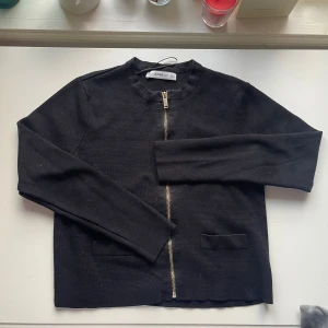 Svart stickad jacka från Zara - Säljer en stilren svart stickad kofta från Zara med dragkedja framtill. Långa ärmar och två dekorationsfickor. Perfekt till alla outfits.