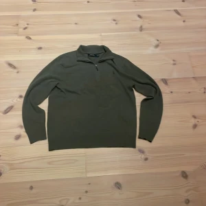 Polo Ralph Lauren Zip - Säljer en stilren olivgrön tröja från Polo Ralph Lauren. Tröjan har en dragkedja vid halsen och är tillverkad i ett mjukt material. Perfekt för kyligare dagar med sin långärmade design.