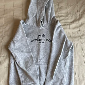Grå hoodie från Peak Performance - Säljer en stilren grå hoodie från Peak Performance med tryck på bröstet. Skicket är helt nytt och aldrig använt. Hör av dig vid intresse! 😊