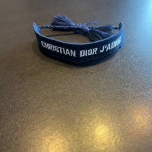 Dior armband - Snyggt blått armband från Christian Dior. Armbandet har en justerbar knytning med tofsar för en personlig passform. Perfekt för att ge en stilren touch till din outfit. Hör gärna av er vid frågor och funderingar🙌