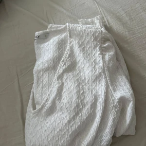 Vit blus med v-ringning - Säljer en stilren vit blus från Only med v-ringning och långa ärmar. Blusen har en texturerad yta och en elastisk midja som ger en smickrande passform. Perfekt för både vardag och speciella tillfällen.