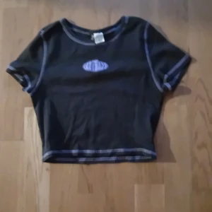 Svart croppad t-shirt - Snygg svart croppad t-shirt med kontrastsömmar och ett litet tryck på bröstet. Perfekt för en avslappnad stil.