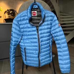 Blå quiltad jacka från Colmar - Snygg blå quiltad jacka från Colmar med dragkedja och långärmade ärmar. Perfekt för kyligare dagar med sin lätta och bekväma design. Jackan har en stilren look med Colmar-logga på ärmen.