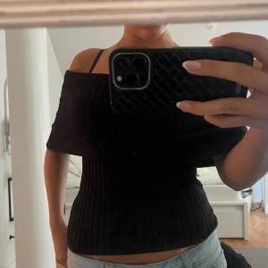 Svart ribbad off-shoulder topp - Säljer en snygg svart ribbad off-shoulder topp. Den är formar sig jättefint men är i väldigt stretchigt å skönt material, perfekt för en utekväll eller fest. Toppen har en stilren design med en bred off-shoulder krage. Passar bra till både jeans och kjol. Använd ett fåtal gånger, så den är i nyskick.