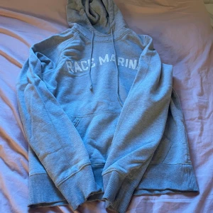 Grå hoodie från Race Marine - Säljer en grå hoodie från Race Marine. Den är supermjuk och bekväm, perfekt för kyliga dagar. Hoodien har en stor ficka på magen och en justerbar huva med dragsko. Texten 'RACE MARINE' är tryckt på bröstet i vitt. Passar perfekt för en avslappnad stil eller för att mysa hemma. 🧥