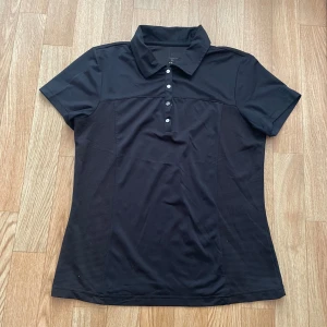 Svart pikétröja från IZOD - Säljer en snygg svart pikétröja från IZOD. Tröjan har en klassisk krage och knappar framtill.  Tröjan har har använts men är i relativt bra skick och redo för en ny ägare🤗