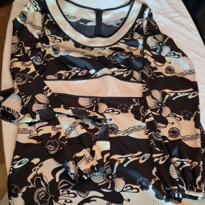 Mönstrad klänning från Lindex - Säljer en superfin mönstrad klänning från Lindex i storlek 40 (M). Klänningen har ett unikt svart och beige mönster med blommor och vågor. Den är långärmad och har en dragkedja i ryggen. Perfekt för både fest och vardag!