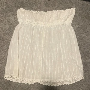 Vit axelbandslös topp med spetsdetaljer - Säljer en söt vit bandeau topp! Har band man kan justera storlek! Lite stor i storleken