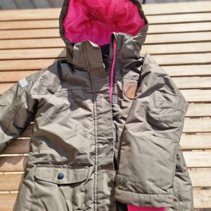 Grön vinterjacka från H&M Sport - Säljer en grön vinterjacka från H&M Sport i storlek 128 (7-8 år). Jackan har en varm och mysig rosa foder på insidan och en huva med rosa insida. Den har en dragkedja framtill och knappar för extra skydd mot kylan. Perfekt för kalla vinterdagar! 🌨️