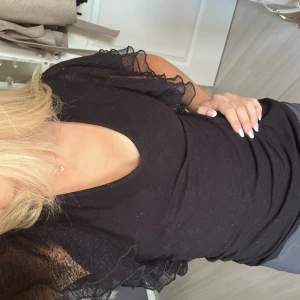 Svart topp med volangärmar från Holly & White - Säljer en snygg svart topp från Holly & White. Den har v-ringning och korta ärmar med volangdetaljer som ger en romantisk touch. Perfekt för både vardag och fest!