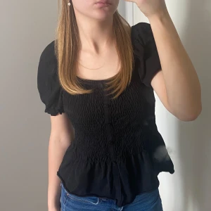 FIN SVART TRÖJA🖤 - En fin svart T-shirt som är räfflad och som går ut längst ner. Puff ärmar. Knappar i mitten, som inte går att öppna. Skriv ifall du har några funderingar ang plagget.😊