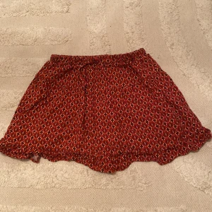 Röd mönstrad kjol från Zara - Säljer en superfin röd kjol från Zara med ett coolt mönster i svart och vitt. Kjolen är kort och har en elastisk midja för en bekväm passform. Perfekt för sommaren eller en fest! Den är i bra skick och redo för en ny ägare. Änvändt den ungefär 2 gånger, men är för liten🌟. Har också inbyggda shorts!