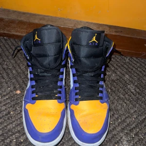 Nike Jordan 1 mid  - Air Jordan 1 Retro High 'Lakers' i lila och gul. Skorna är i gott skick med normala tecken på användning.