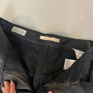Svarta skinnbyxor från Levi's - Säljer ett par svarta skinnbyxor från Levi's i storlek 25. Byxorna har en hög midja och en flare-stil som ger en snygg siluett. Perfekta för en cool och edgy look! 🖤