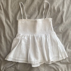 Vit ärmlös topp med smockdetaljer - säljer denna söta topp ifrån Gina tricot. banden går att ta av om man hellre vill ha den som en tubtopp. storleken är 146/152 men den passar mig som är 162 och brukar ha xs/s i toppar. pris kan diskuteras💓