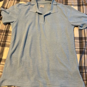 Ljusblå pikétröja från Jack & Jones - Säljer en snygg ljusblå pikétröja från Jack & Jones. Tröjan är i storlek L och är perfekt för både vardag och lite mer uppklädda tillfällen. Den är tillverkad i ett bekvämt material som känns skönt mot huden. Tröjan har korta ärmar och en klassisk krage med knappar. Passar perfekt till jeans eller chinos!