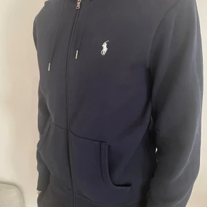 Ralph Lauren Zip Hoodie - Säljer nu denna mörk blåa Ralph Lauren zip hoodien i fint skick. Säljer för att den inte kommer till användning. Köpt på deras hemsida. Kan tänka att gå ner i pris vid snabb affär. Tveka inte på att höra av er om det finns några funderingar!  