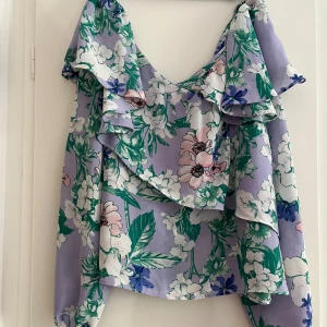 Blommig off-shoulder topp med volanger - Säljer en superfin off-shoulder topp med blommigt mönster i lila, grönt och rosa. Toppen har volanger som ger en romantisk känsla och är perfekt för sommaren. 