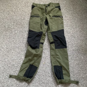 Gröna och svarta cargopants från 157 - Säljer ett par gröna och svarta cargopants från 157 i storlek Small. Byxorna har flera praktiska fickor med dragkedjor och förstärkta partier i svart tyg. De har en normal passform och justerbara benslut för bästa komfort. Perfekta för utomhusaktiviteter eller vardagsbruk. köparen betalar för frakt!