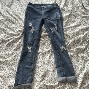 Blå jeans med slitningar - Snygga blå jeans med slitningar på benen och uppvikta benslut. Perfekta för en avslappnad stil. De har en klassisk femficksdesign och knappgylf. 