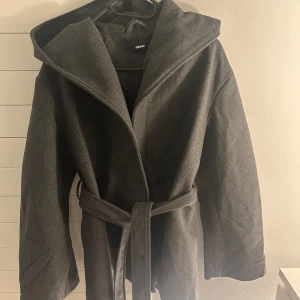 Grå kappa från BikBok - Snygg grå kappa från BikBok i storlek XS. Den har en huva och ett knytskärp i midjan för en stilren look.🩷🩷