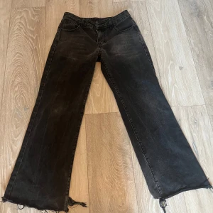 Svarta jeans med slitna detaljer - Säljer ett par svarta jeans med fransiga och slitna detaljer vid bensluten. Byxorna har en rak passform och är tillverkade i ett robust denimtyg. Perfekta för en avslappnad stil.