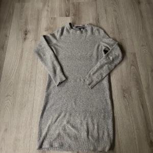 Grå stickad klänning - Säljer en mysig grå stickad klänning med långärmad design. Perfekt för kyligare dagar med sin mjuka och bekväma passform. Klänningen har en enkel och stilren look som passar till många tillfällen. fint skick! använd fåtal gånger🫶🏼