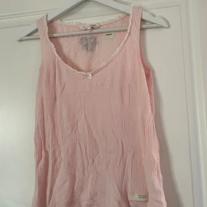 Rosa linne från Odd Molly - Sött rosa linne från Odd Molly med en liten rosett framtill och spetsdetaljer längs halsringningen. Toppen har en lätt ribbad struktur och ett litet märke nertill. Perfekt för en avslappnad stil. Passar perfekt till vår/sommargarderoben! Linnet är i fint skick och sparsamt använt. Vid frågor och funderingar hör av er, jag svarar så fort jag kan!🩷