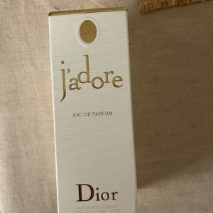 J'adore Eau de Parfum från Dior - Elegant parfymflaska från Dior med en ikonisk design. Flaskan är genomskinlig med en gyllene hals och en rundad topp. J'adore är en klassisk doft som utstrålar lyx och femininitet. Perfekt för den som vill ha en tidlös och sofistikerad parfym.