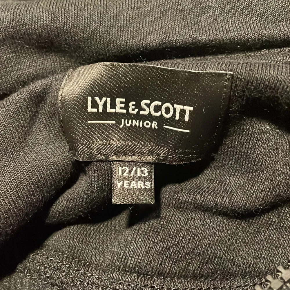 Säljer en svart hoodie från Lyle & Scott Junior. Den har en praktisk dragkedja framtill och en känguruficka. På ärmen finns en broderad logotyp i gult. Perfekt för en stilren och bekväm look. Köpt på Lyle & Scott.. Neuletakit & Villapaidat.