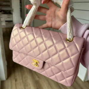 Rosa quiltad axelväska - Snygg rosa axelväska med quiltat mönster och gulddetaljer. Väskan har en klassisk design med en elegant kedja och ett ikonisk märke på framsidan. Perfekt för att ge din outfit en lyxig touch.