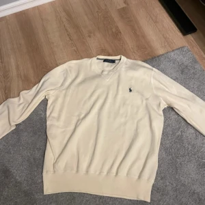 Cremevit crewneck sweater från Ralph Lauren - Säljer en stilren cremevit crewneck sweatshirt från Polo Ralph Lauren. Tröjan har en klassisk  design och det ikoniska logotypbroderiet på bröstet. Perfekt för en elegant och avslappnad look.