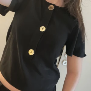 Svart kortärmad topp med knappar - Snygg svart topp med korta ärmar och dekorativa guldknappar framtill. Från Zaras trf kollektion. 